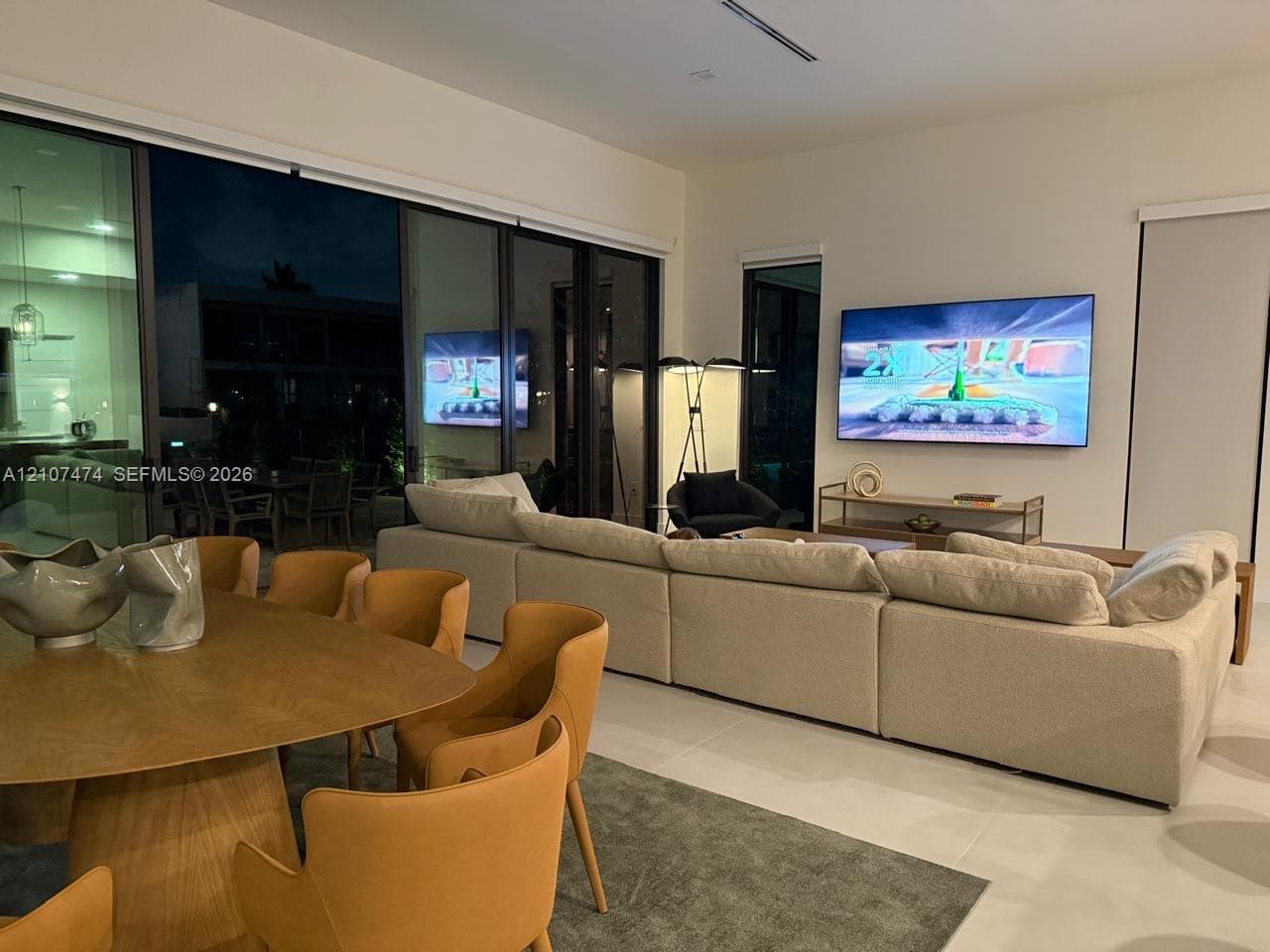 Open-concept living space featuring floor-to-ceiling multi-panel sliding glass doors, neutral tile flooring, and recessed ceiling lighting