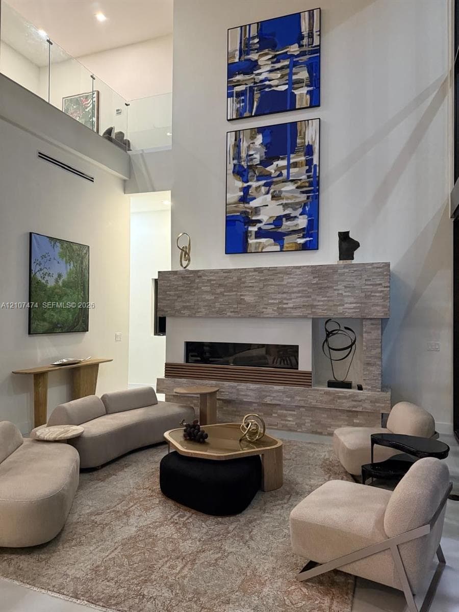 Double-height ceiling, floor-to-ceiling stone-faced fireplace, linear glass-enclosed firebox, and glass panel balcony railing