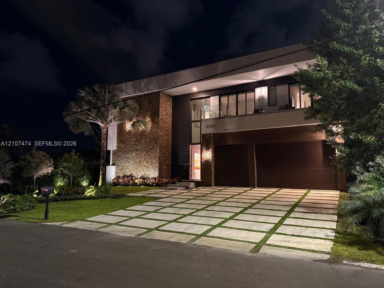 Contemporary exterior featuring textured stone masonry, a two-car garage, multi-level glass balcony railings, and a geometric concrete paver driveway