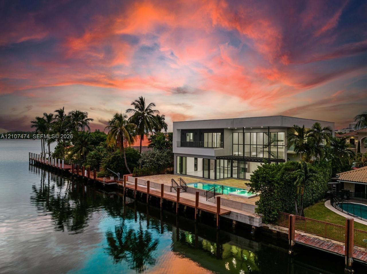Modern waterfront estate featuring floor-to-ceiling windows, a private dock, an inground swimming pool, and stone patio surfacing