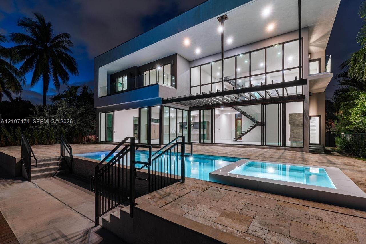 Modern two-story architectural exterior with floor-to-ceiling glass paneling, integrated swimming pool with tiered stone decking, structural pergola, and glass-railed balconies