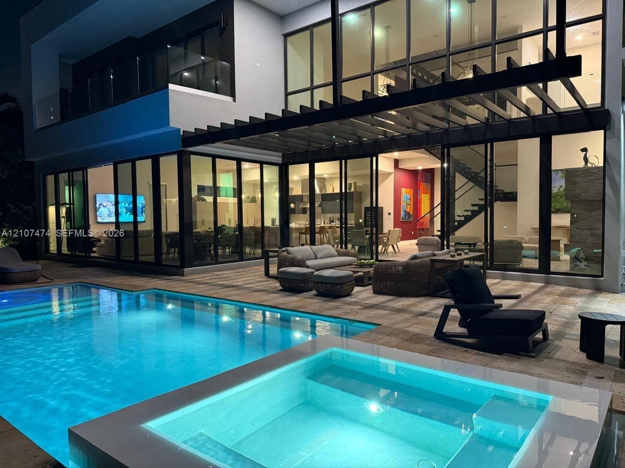 Modern architectural exterior featuring floor-to-ceiling glass panel walls, a multi-level structure with a glass balcony railing, a custom pergola, and an integrated pool and spa area with stone-finish decking