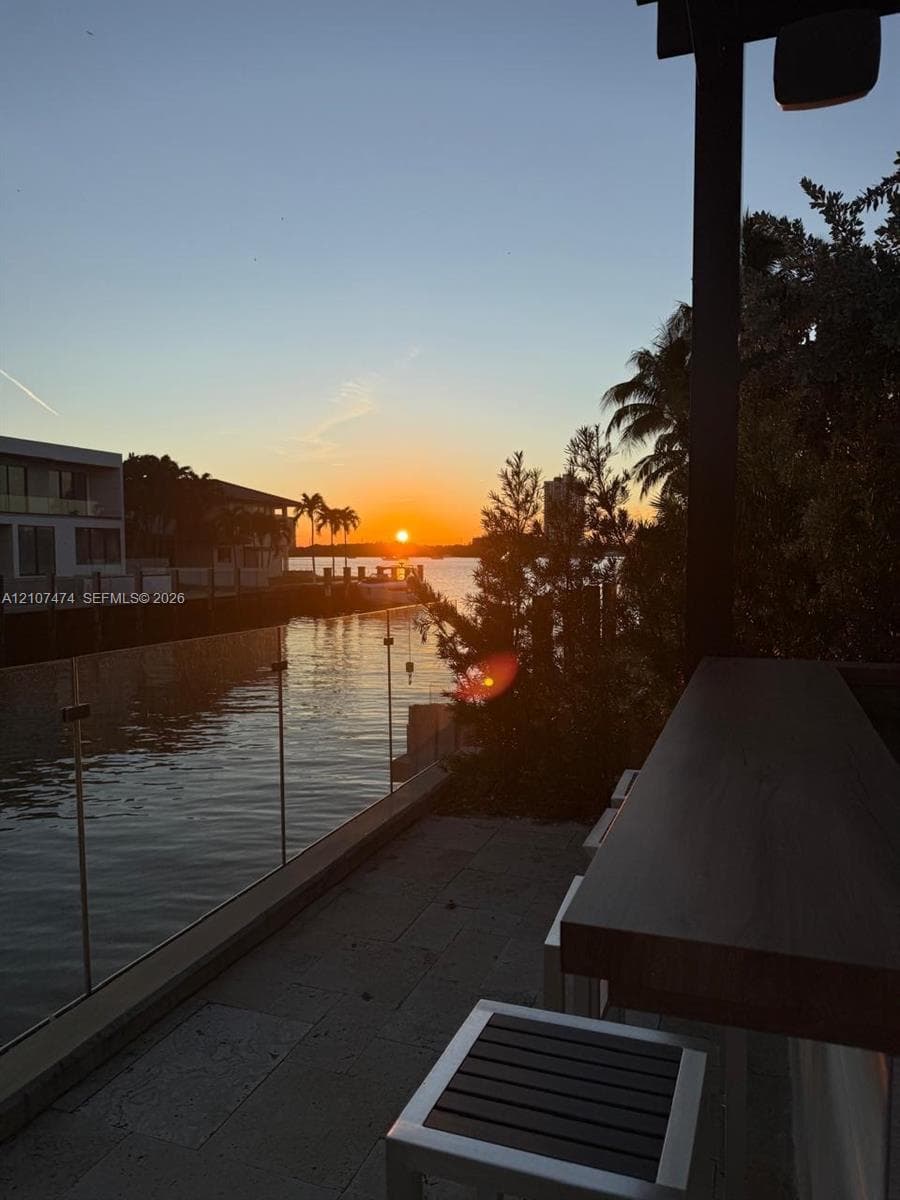 Waterfront terrace featuring stone paver flooring, glass railing, and a built-in exterior bar