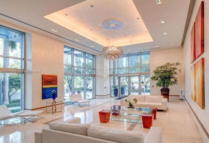 Expansive lobby featuring double-height ceilings, recessed lighting, polished stone flooring, floor-to-ceiling glass paneling, and a centralized decorative pendant fixture