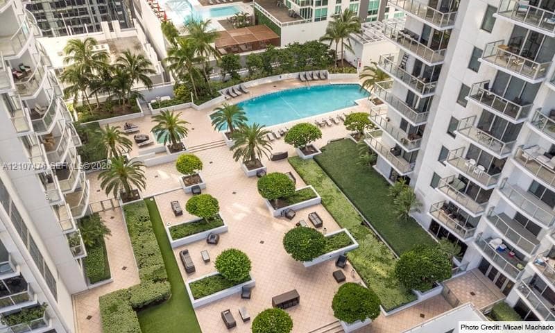 Outdoor common area featuring a swimming pool, paved sun deck, structured landscaping with manicured trees, and private balconies with glass railings