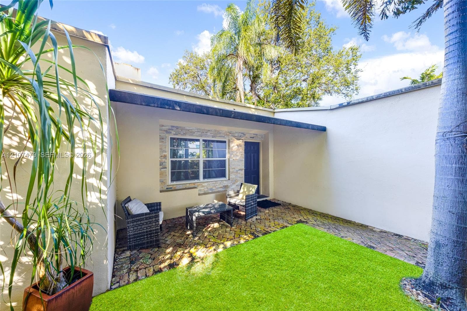 Enclosed outdoor space featuring a paved brick patio, synthetic turf lawn, stone-accented exterior wall, and a covered entry