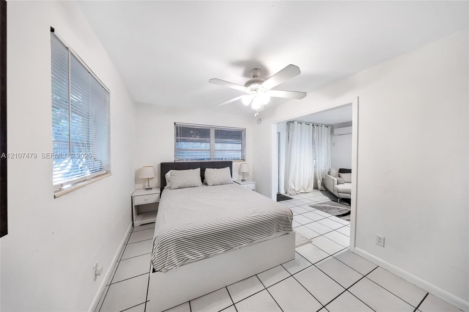 Interior space featuring large-format ceramic floor tiling, white walls, two windows with integrated blinds, and a central ceiling fan with integrated light fixture