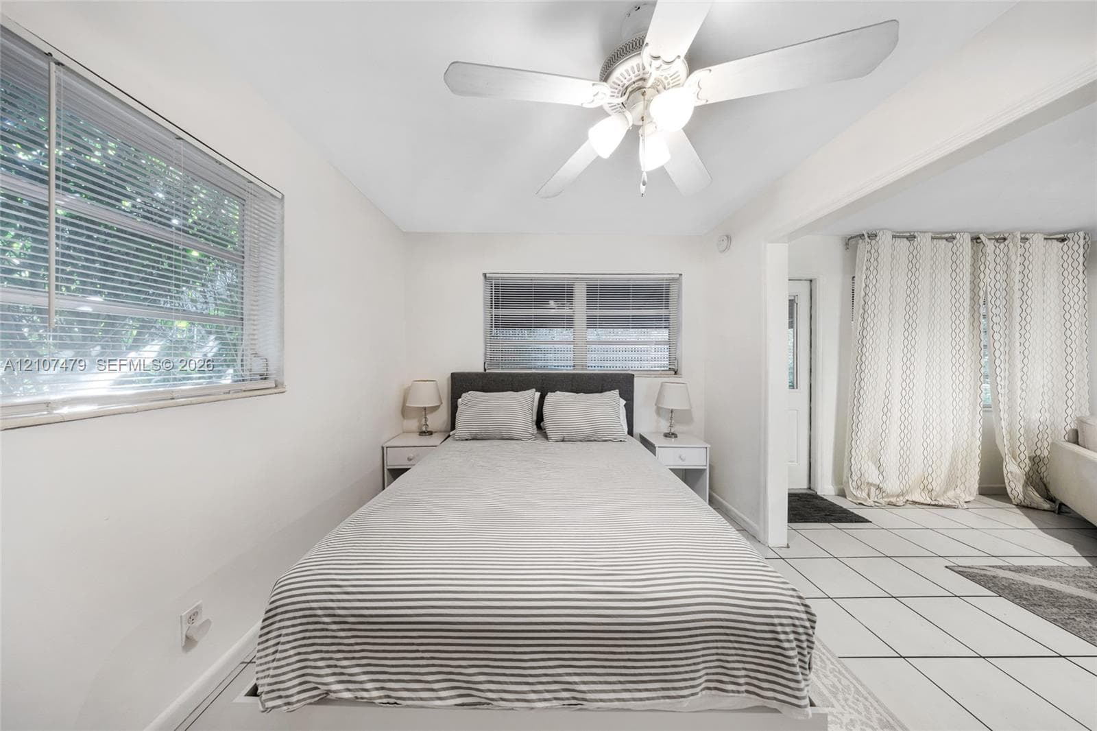 Neutral-toned room featuring a white ceiling fan with integrated lighting, dual horizontal windows, and large-format tile flooring