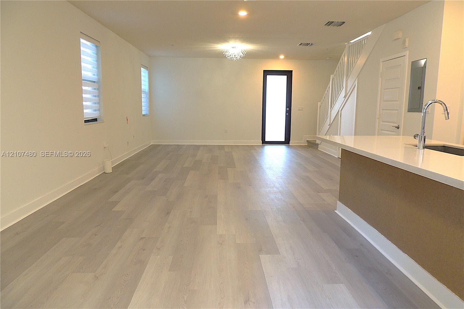 Open-concept interior featuring light wood-finish flooring, a kitchen island with stone-surface countertop, recessed lighting, and a staircase with decorative railing