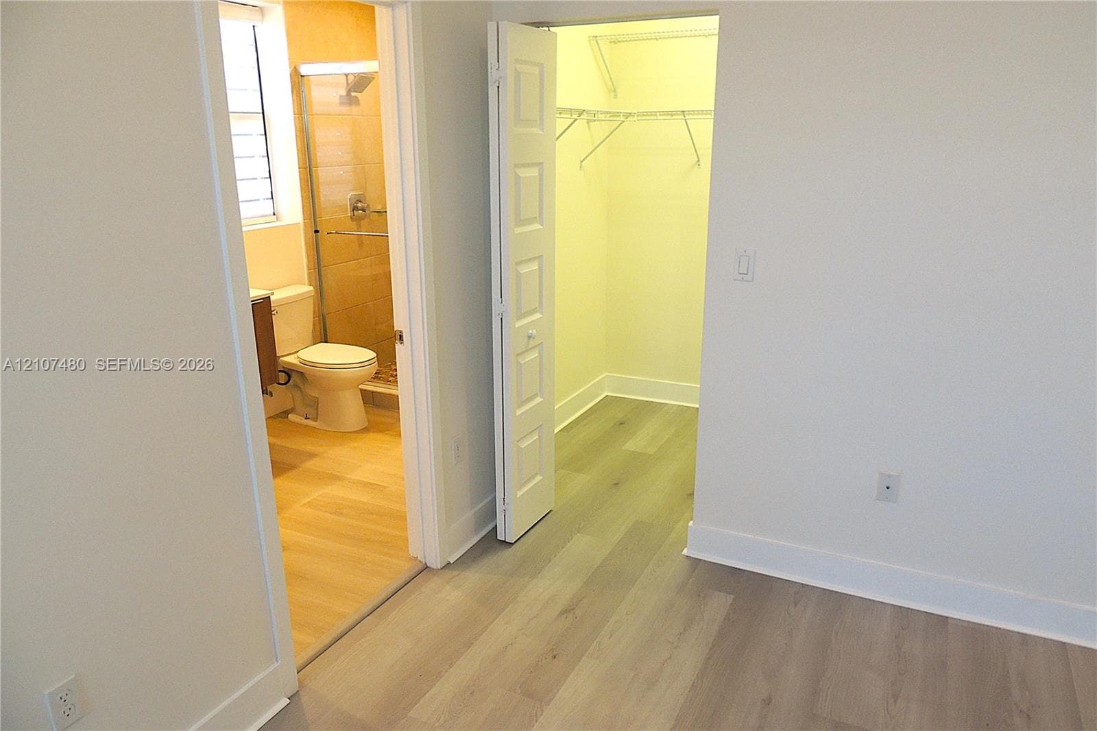 Wood-finish flooring, walk-in closet with integrated shelving, and bathroom featuring a glass-enclosed shower and tile flooring