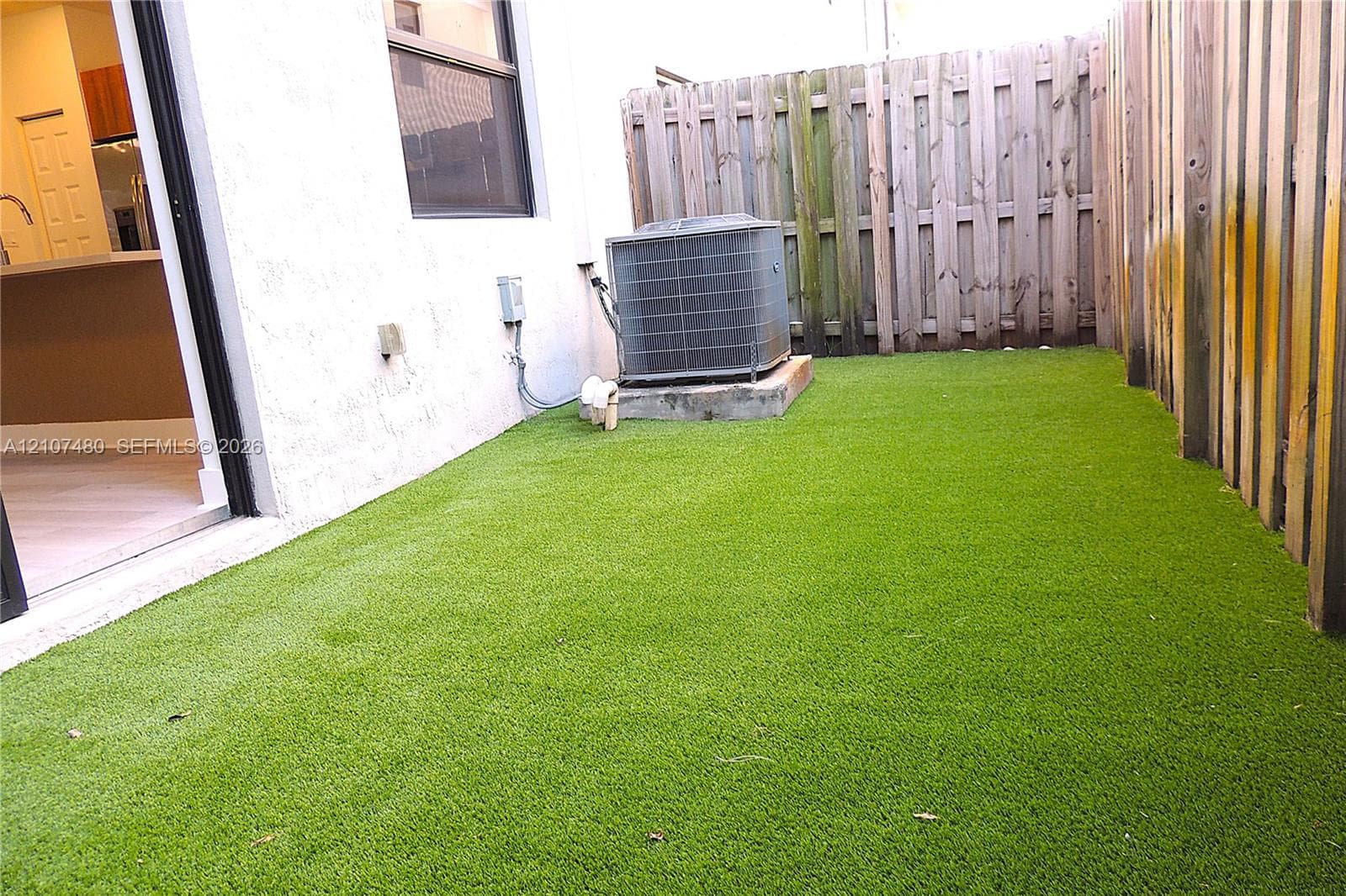 Fenced backyard featuring synthetic turf and an exterior HVAC unit
