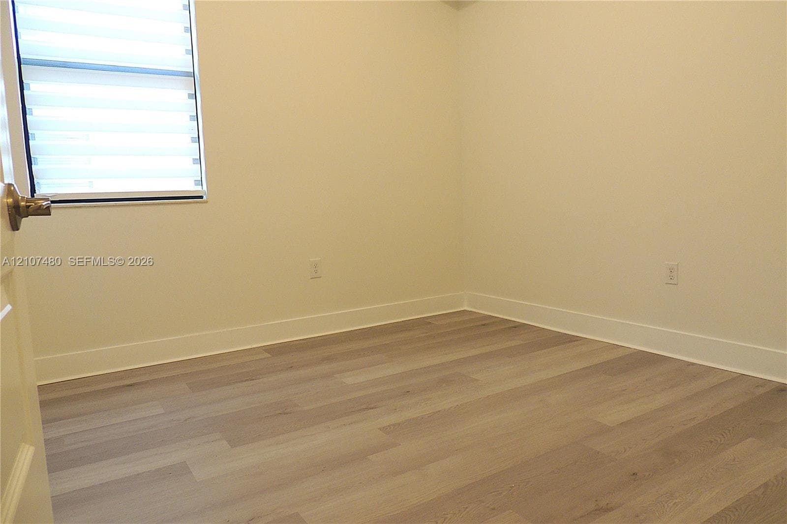 Wood-finish flooring, neutral wall tones, and a window fitted with horizontal blinds