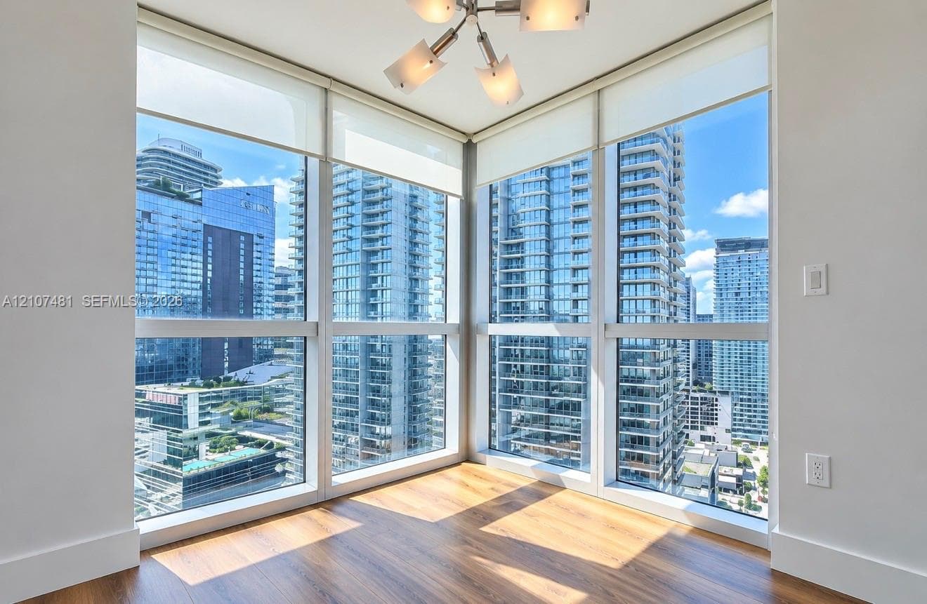 Floor-to-ceiling corner windows, wood-finish flooring, and a modern multi-arm light fixture