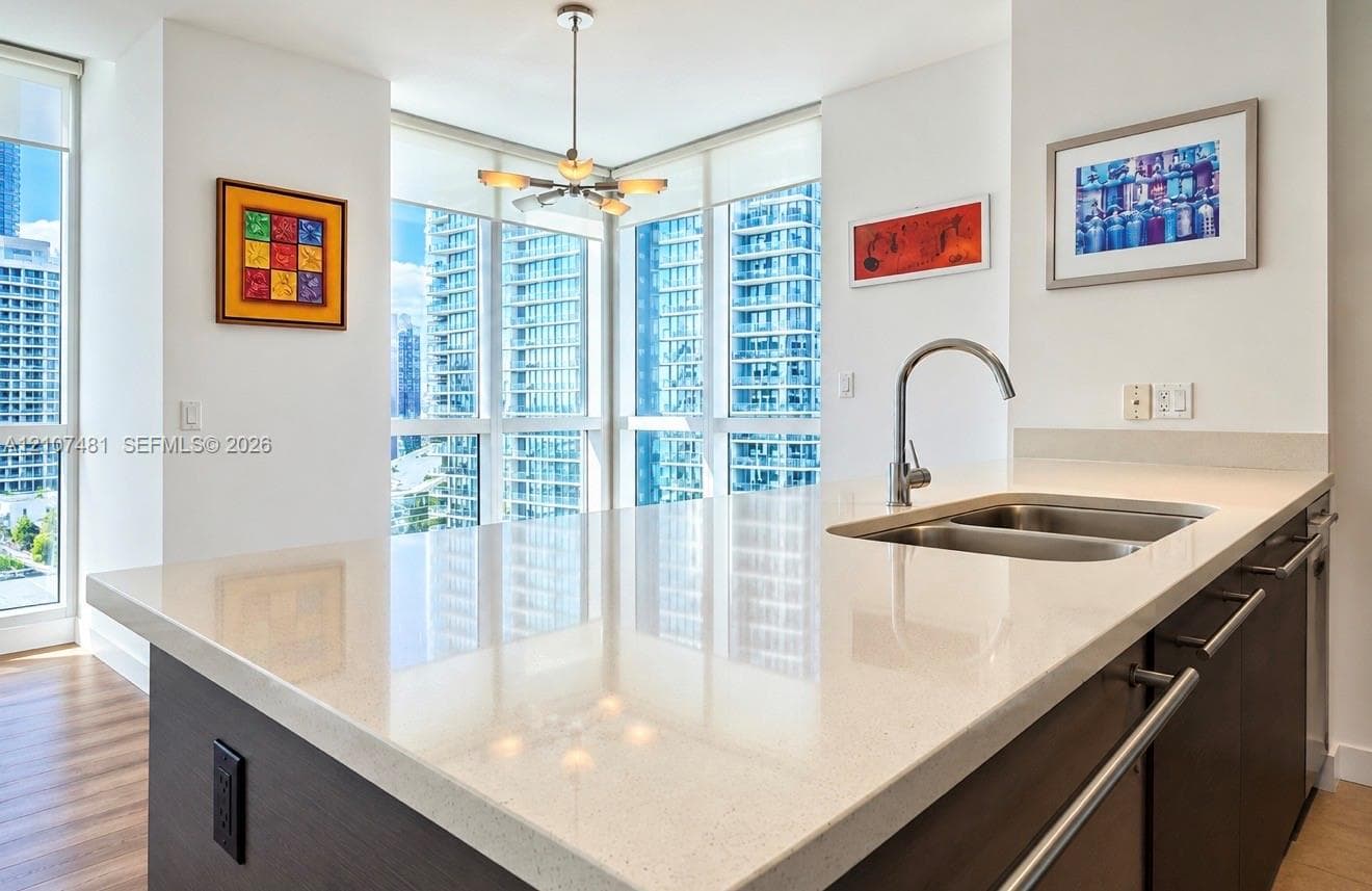 Kitchen island featuring a stone-surface countertop, double-basin stainless steel undermount sink, gooseneck faucet, dark-finish cabinetry, and floor-to-ceiling windows
