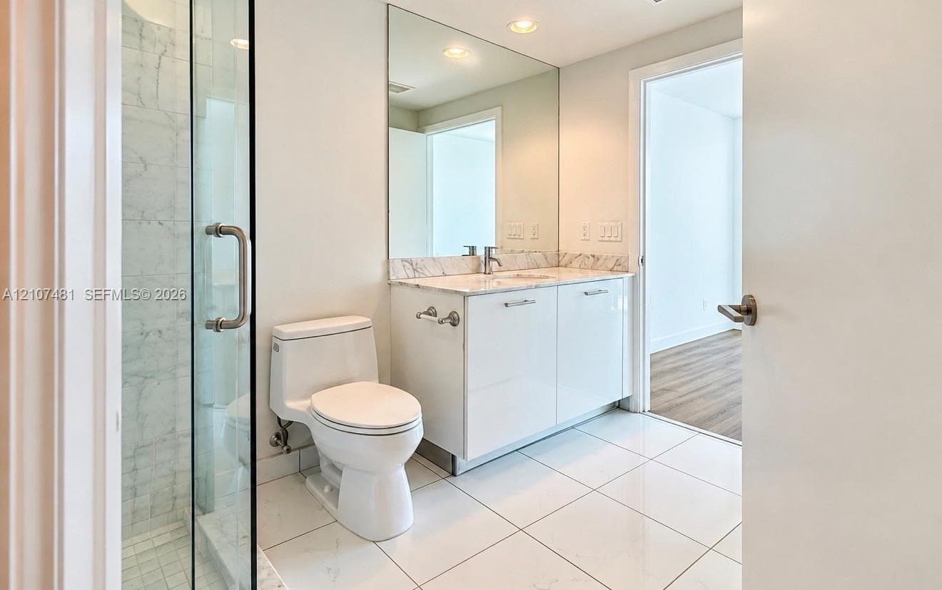 Bathroom featuring a glass-enclosed shower, stone-finish countertop, white cabinetry, wall-to-wall vanity mirror, and large-format tile flooring