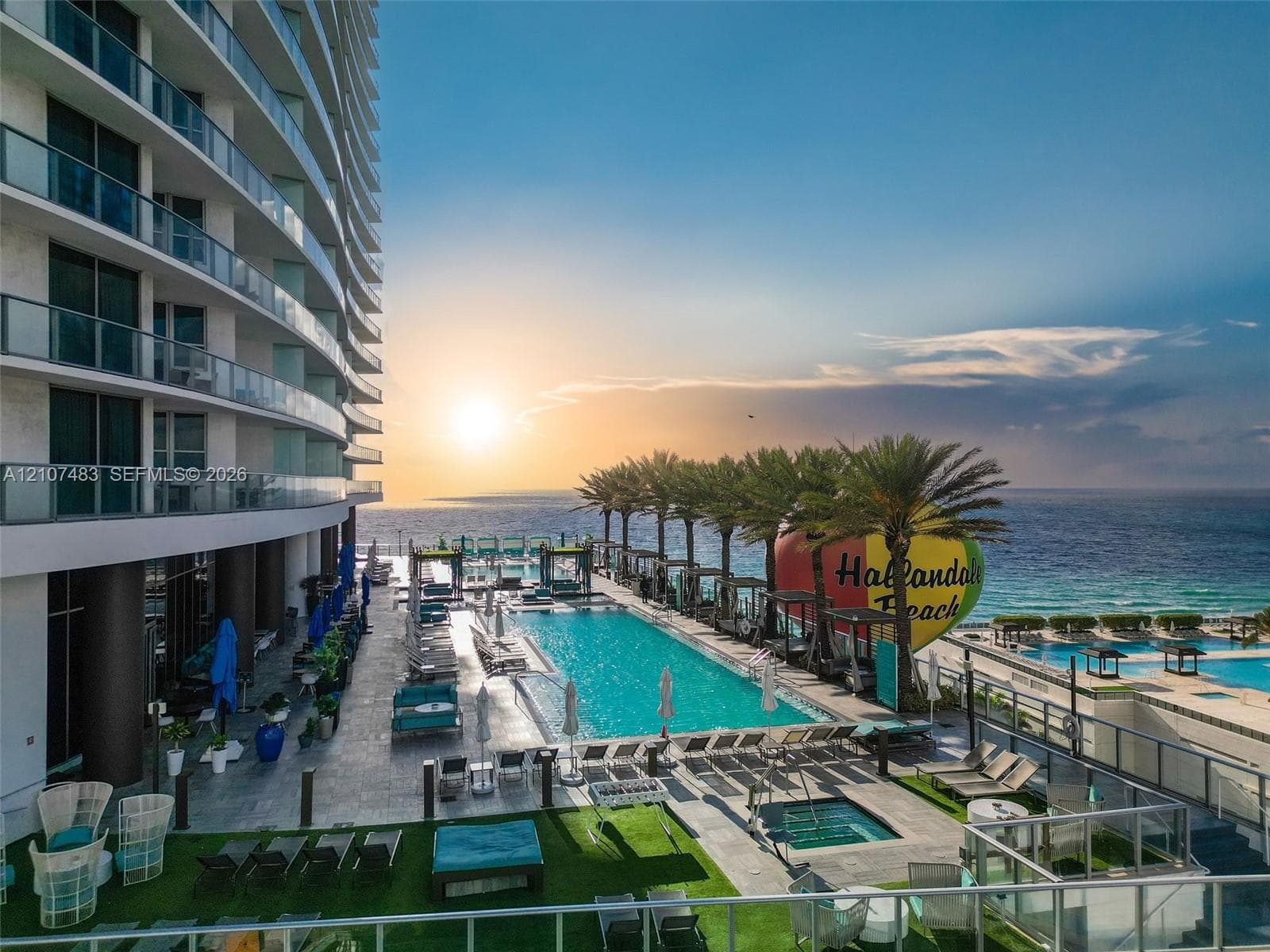 Oceanfront pool area featuring an expansive sundeck, multiple palm trees, and an integrated spa