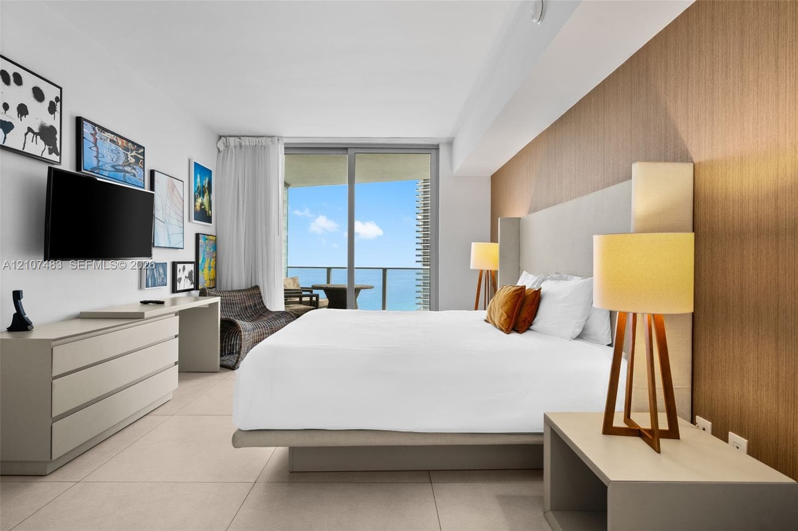 Floor-to-ceiling glass sliding doors opening to an exterior balcony, wood-finish accent wall paneling, large-format tile flooring, and custom built-in cabinetry