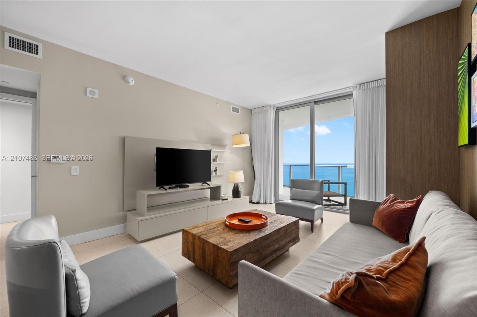 Living area featuring floor-to-ceiling glass sliding doors, ocean backdrop, built-in wall cabinetry, and large-format tile flooring