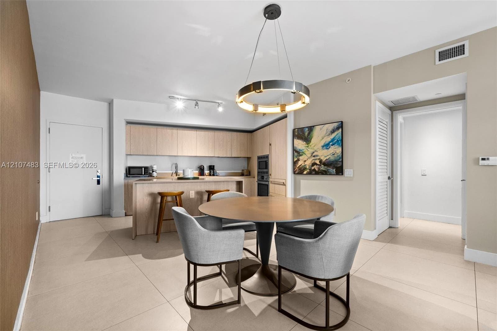 Kitchen featuring light-finish cabinetry, built-in wall oven, and a breakfast bar, complemented by a contemporary circular pendant light and tile flooring