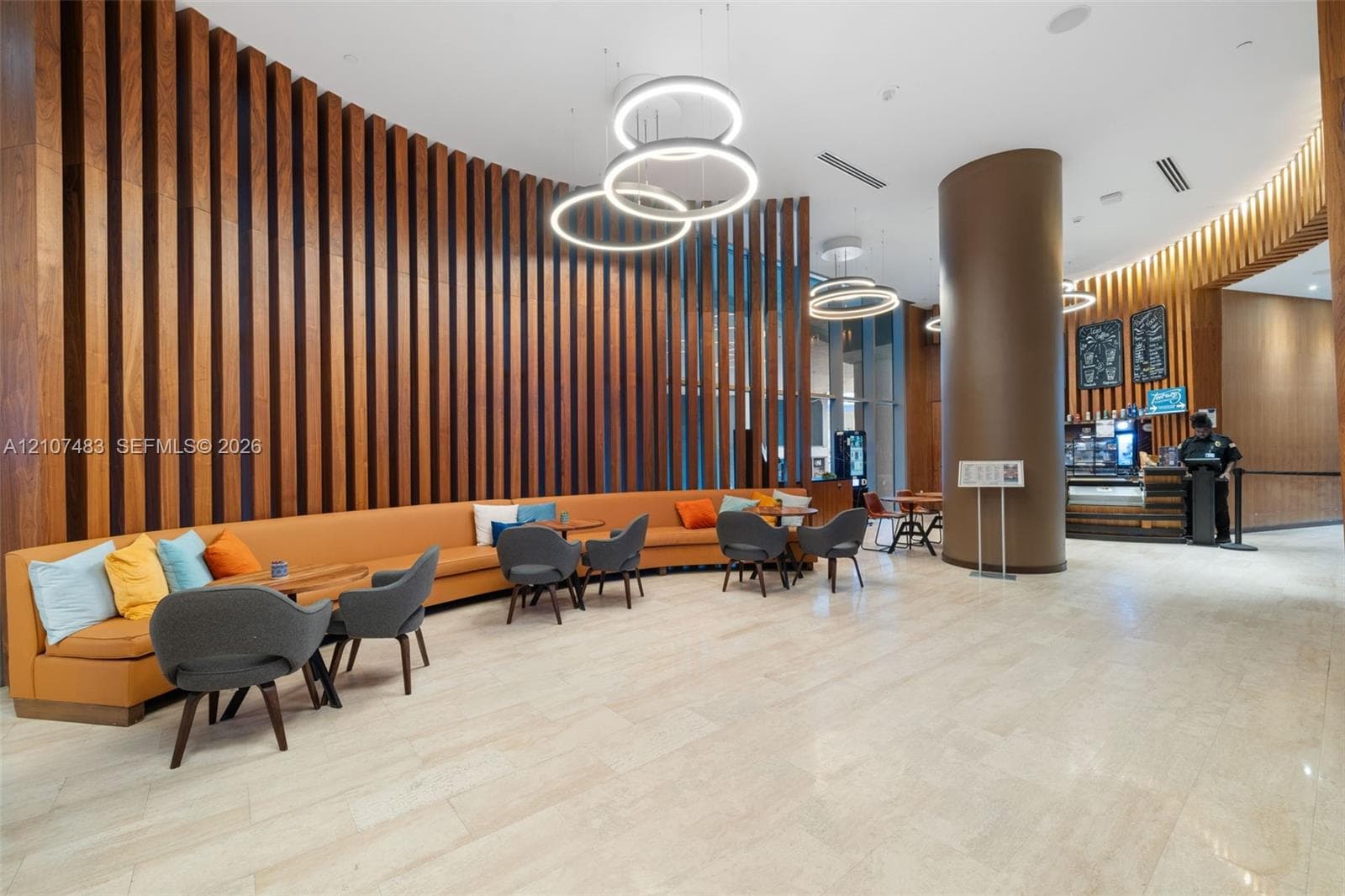 Expansive lobby area featuring a full-height vertical wood-slat accent wall, polished stone flooring, custom circular ring lighting fixtures, and a prominent curved structural column