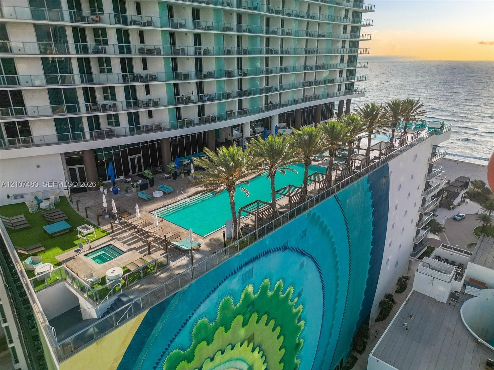 Elevated terrace featuring a swimming pool, integrated spa, artificial turf area, and structural mural, overlooking the ocean