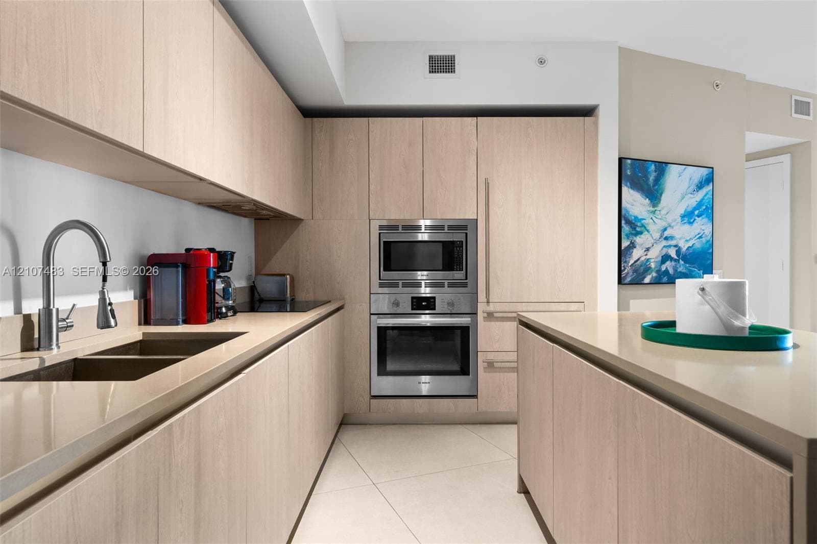 Kitchen featuring light-finish wood cabinetry, integrated stainless steel oven and microwave, stone-finish countertops, and an undermount dual-basin sink with a high-arch faucet