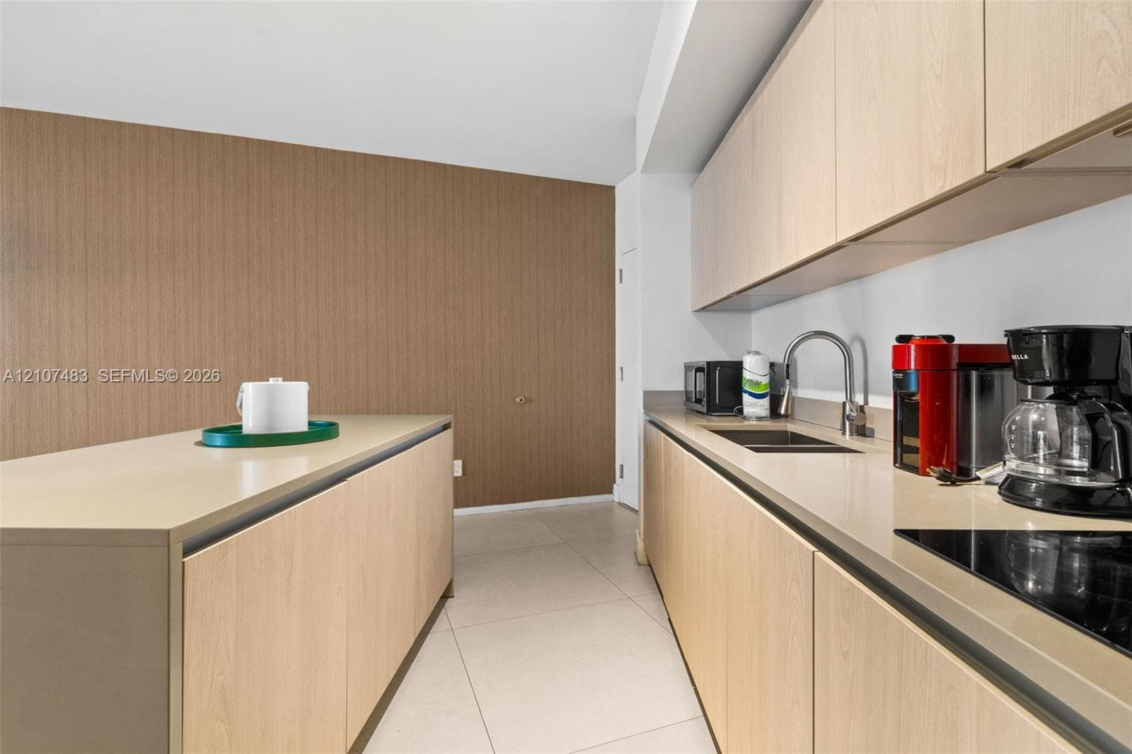 Contemporary kitchen featuring light wood-finish cabinetry, sleek solid-surface countertops, an undermount stainless steel sink, a smooth-top cooktop, and large-format tile flooring