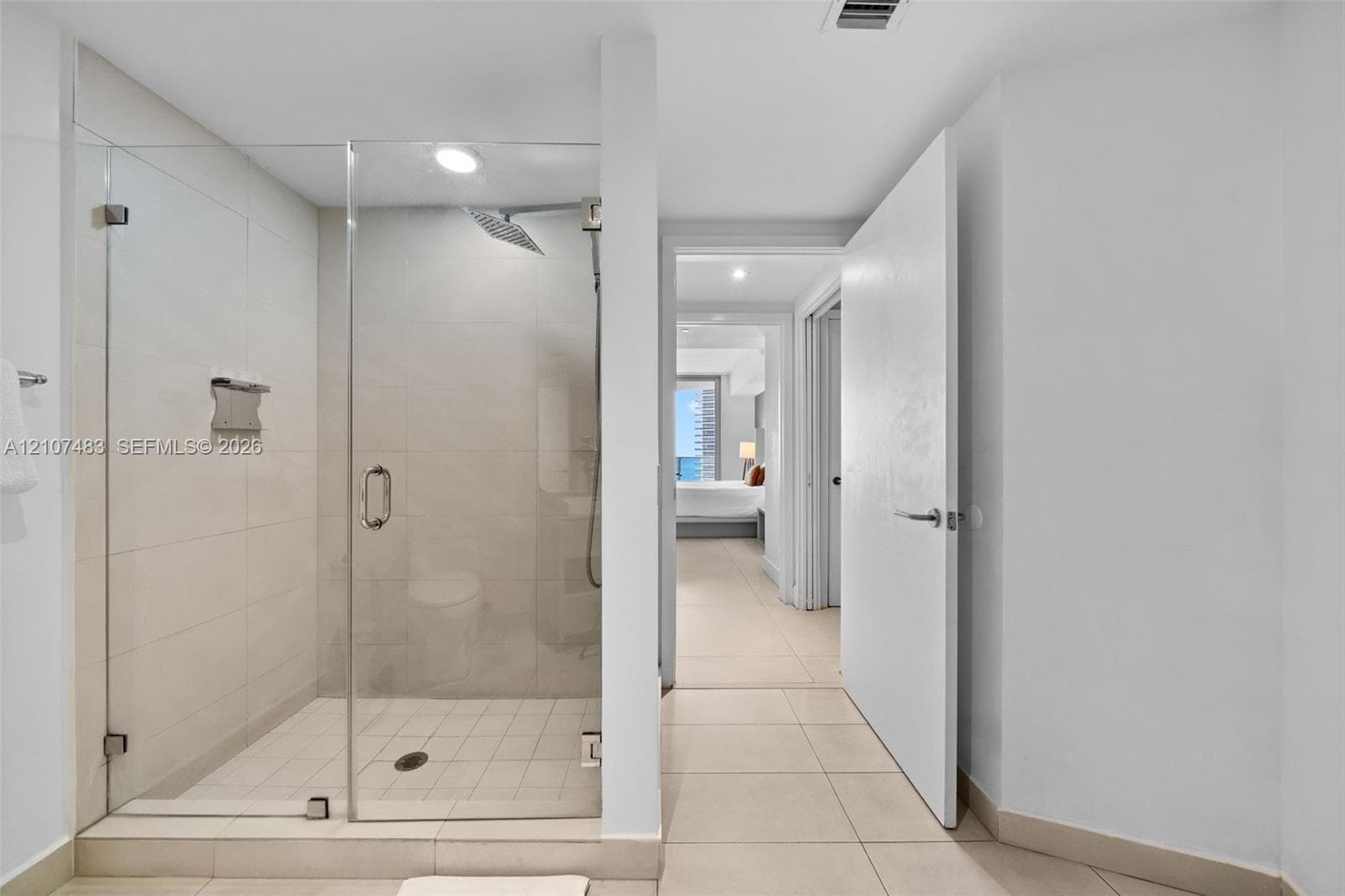 Walk-in shower featuring a glass enclosure, large-format tile surround, rainfall shower head, and built-in metal shelving, complemented by light-toned tile flooring
