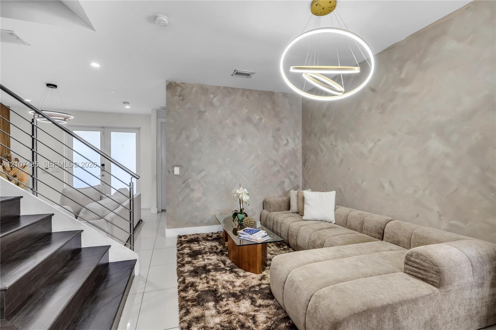 Staircase featuring wood-finish treads and a horizontal cable railing system, polished large-format tile flooring, textured accent wall, and a contemporary multi-ring pendant light fixture
