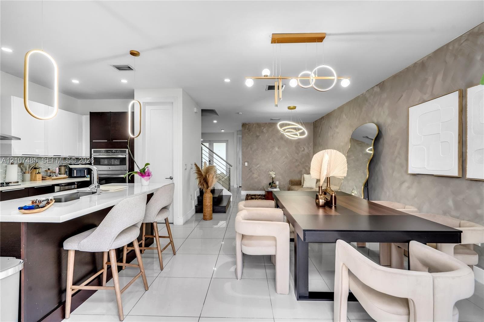 Open-concept kitchen featuring high-gloss cabinetry, a spacious island with a stone-finish countertop, large-format tile flooring, textured accent walls, and custom modern pendant lighting