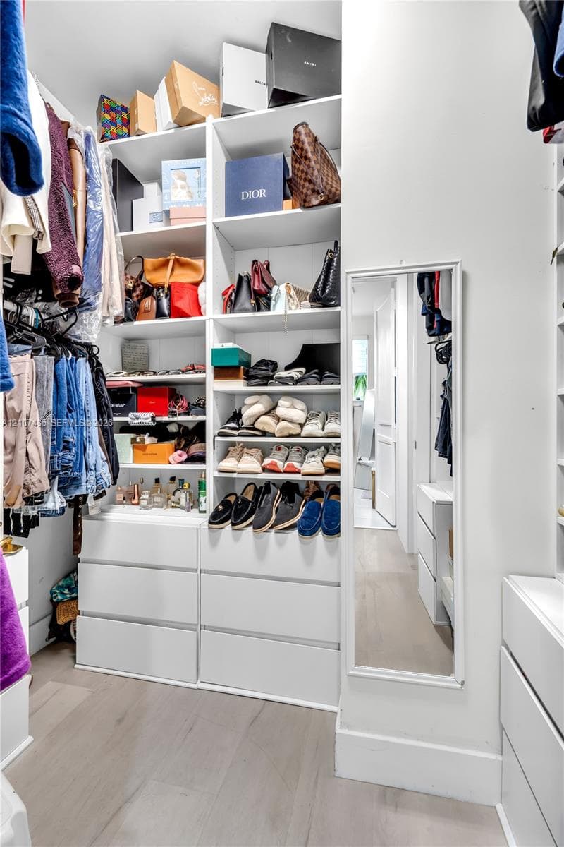 Walk-in closet featuring white custom built-in shelving, floor-to-ceiling storage units, multiple integrated drawer banks, and light-toned wood-finish flooring