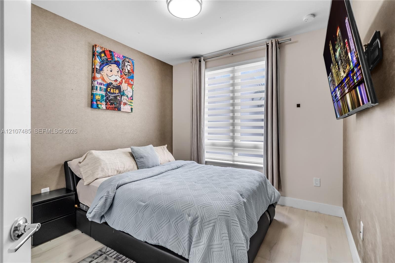 Neutral-toned wall finish, wood-finish flooring, and large window featuring dual-layered adjustable blinds, illuminated by a flush-mount overhead light fixture