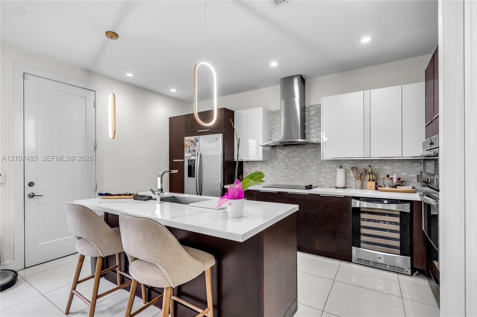Kitchen featuring two-tone cabinetry, quartz countertops, a central island with an undermount sink, built-in wine cooler, and stainless steel range hood