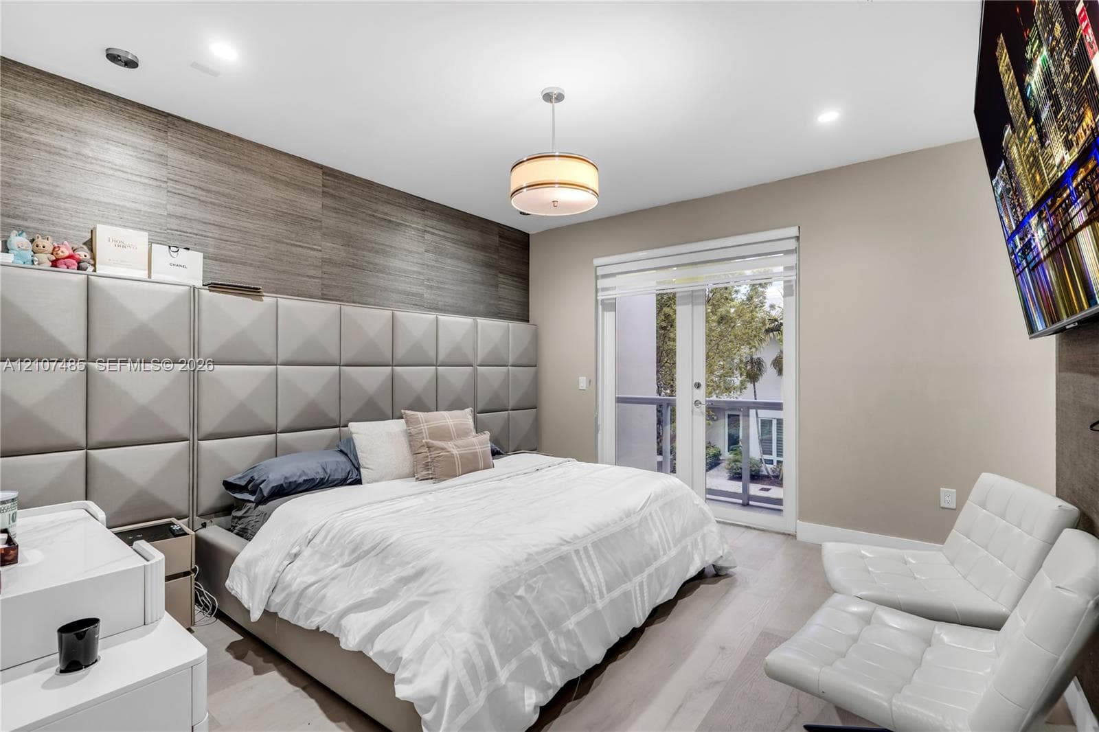 Custom upholstered wall paneling, wood-finish flooring, recessed lighting, central pendant fixture, and glass-paneled exterior door