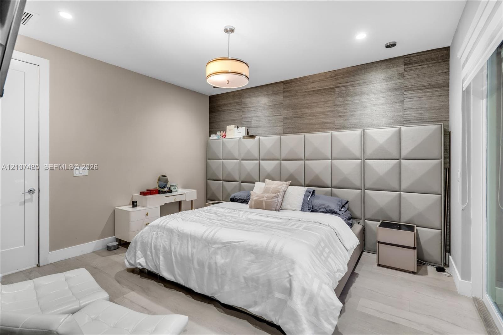 Custom wall-mounted upholstered grid headboard, horizontal wood-texture wall paneling, drum pendant light fixture, recessed ceiling lighting, and wood-finish flooring