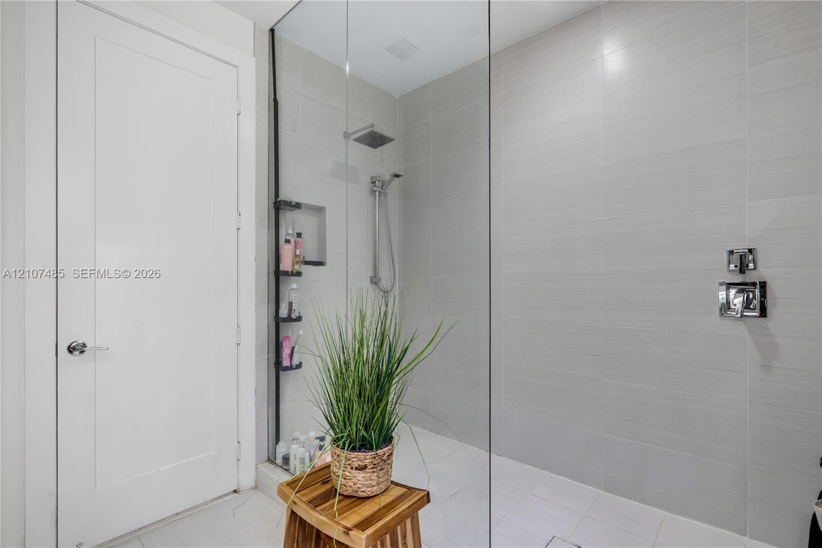 Walk-in shower featuring floor-to-ceiling ceramic tile, frameless glass enclosure, built-in recessed storage niche, and polished chrome rainfall showerhead with handheld attachment