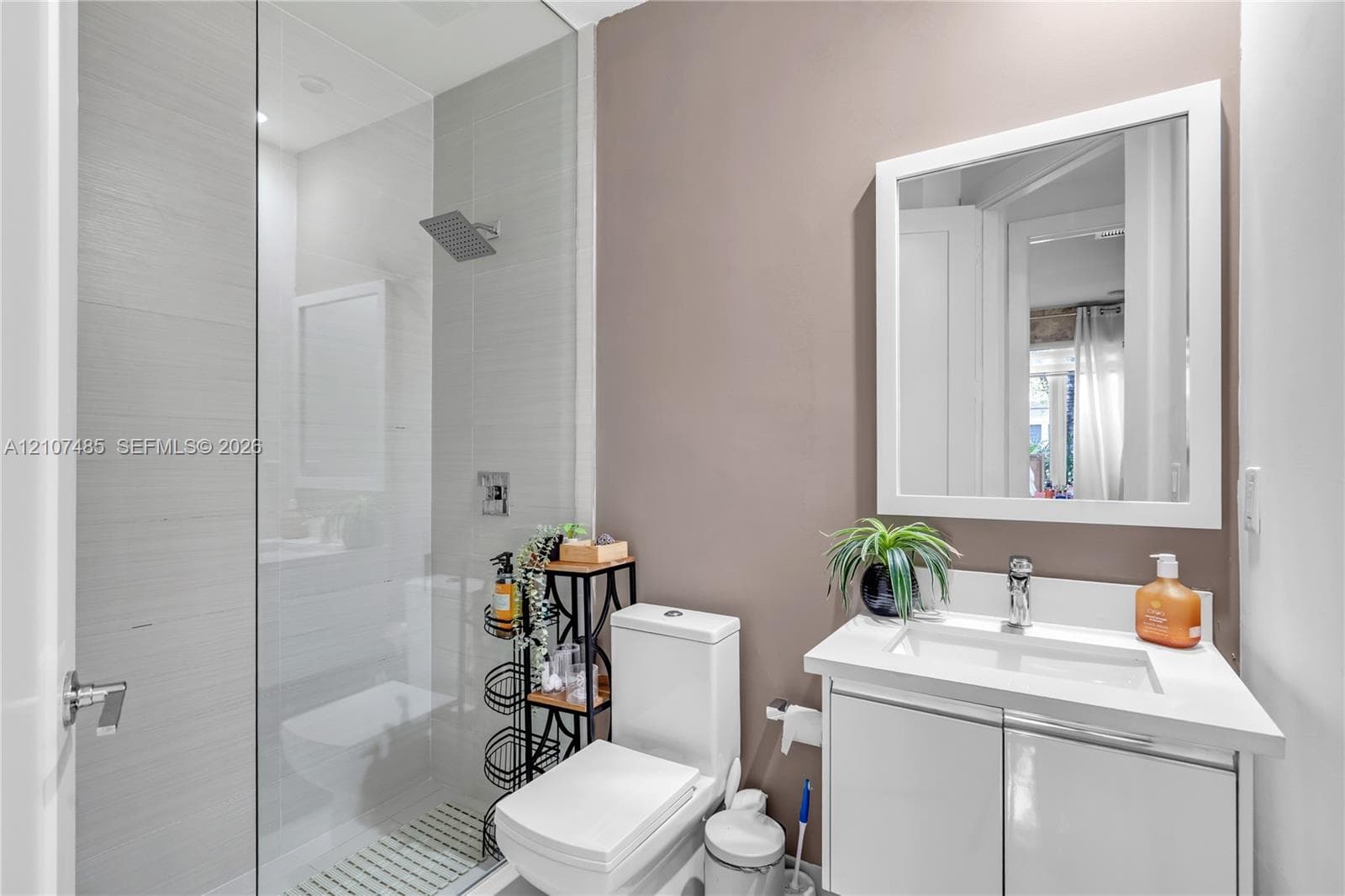 Bathroom featuring a glass-enclosed shower with horizontal wall tile, rainfall showerhead, white vanity with an integrated rectangular sink, and a framed wall mirror