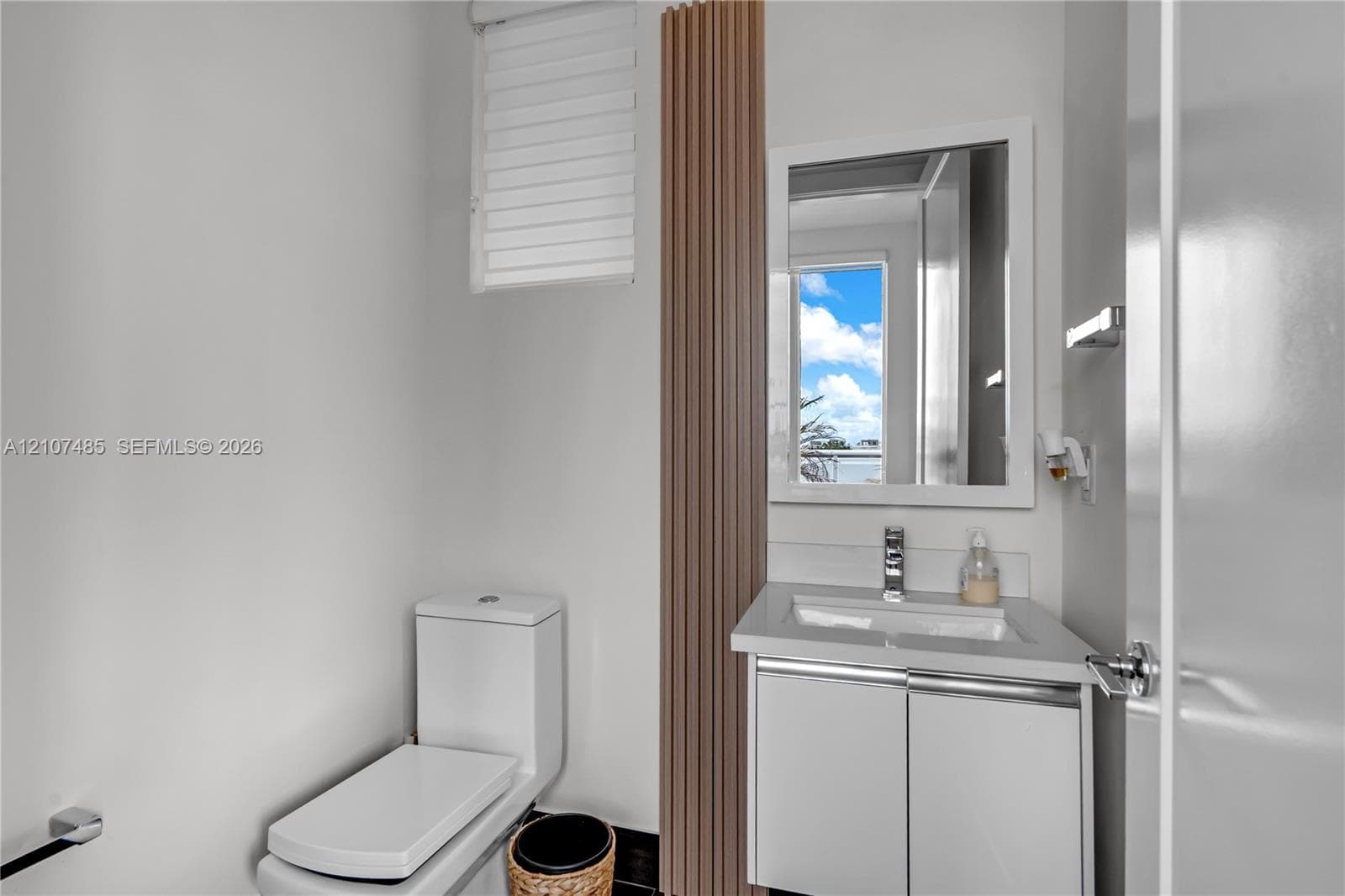 Compact vanity with stone-composite countertop, undermount sink, chrome faucet, vertical wood-slat accent panel, and wall-mounted mirror