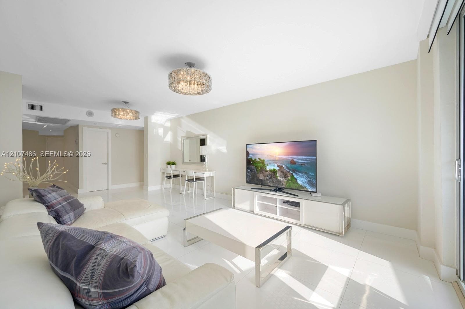 Open-concept living space featuring high-gloss tile flooring, dual contemporary drum-style pendant light fixtures, and sliding glass doors