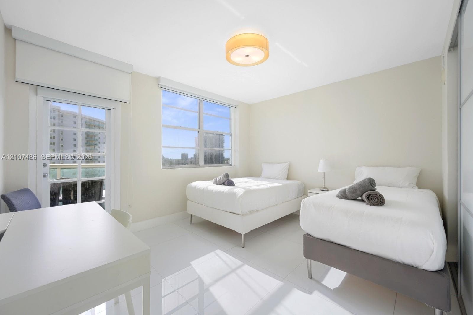 Bright room featuring polished white tile flooring, neutral wall tones, a central drum-style ceiling light fixture, large windows, and a glass-paneled door with an integrated exterior balcony