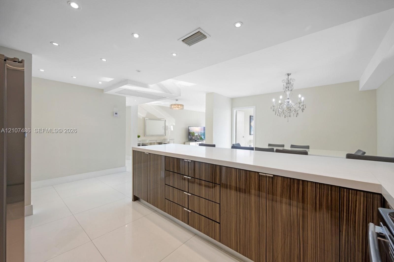 Kitchen island featuring high-gloss wood-grain cabinetry, quartz countertops, large-format tile flooring, recessed ceiling lighting, and a tiered crystal chandelier