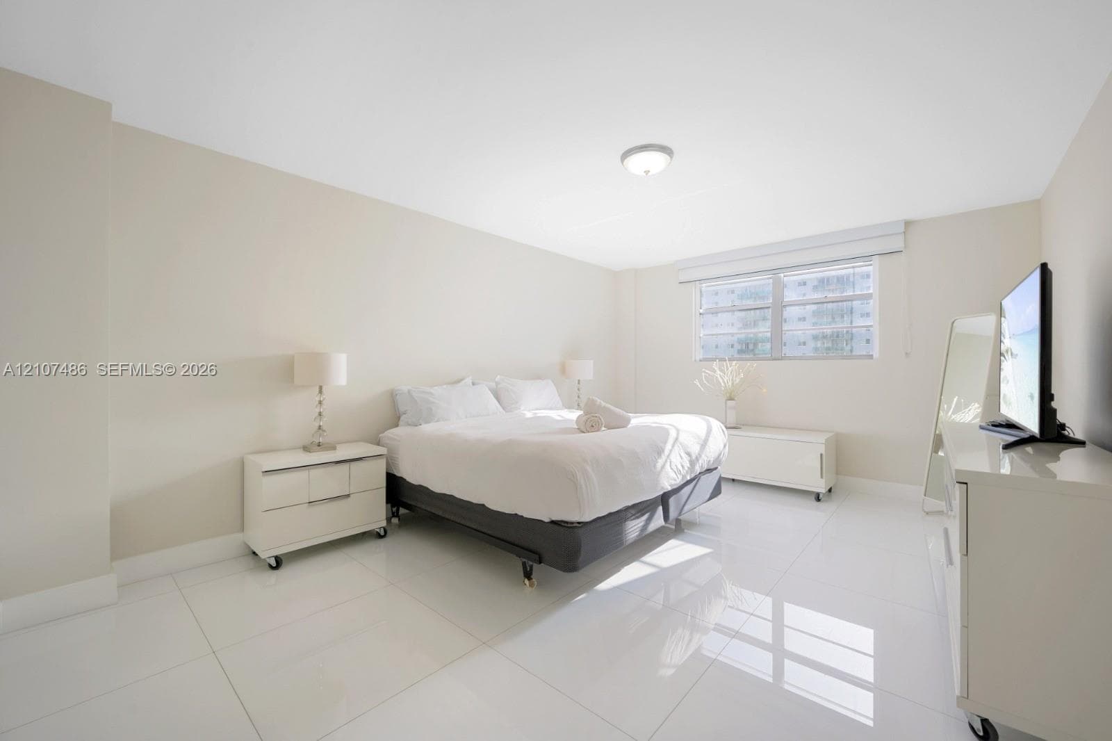 Spacious room featuring polished tile flooring, neutral wall tones, flush-mount ceiling lighting, and a large window with fitted blinds