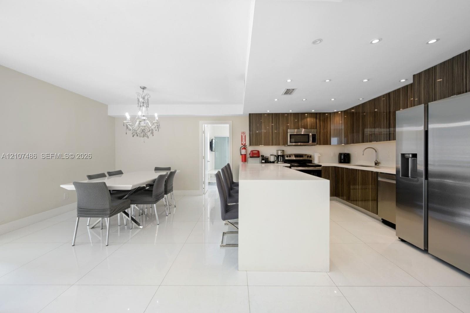 Kitchen featuring high-gloss cabinetry, stone-surface breakfast bar, polished tile flooring, stainless steel appliances, and crystal chandelier lighting