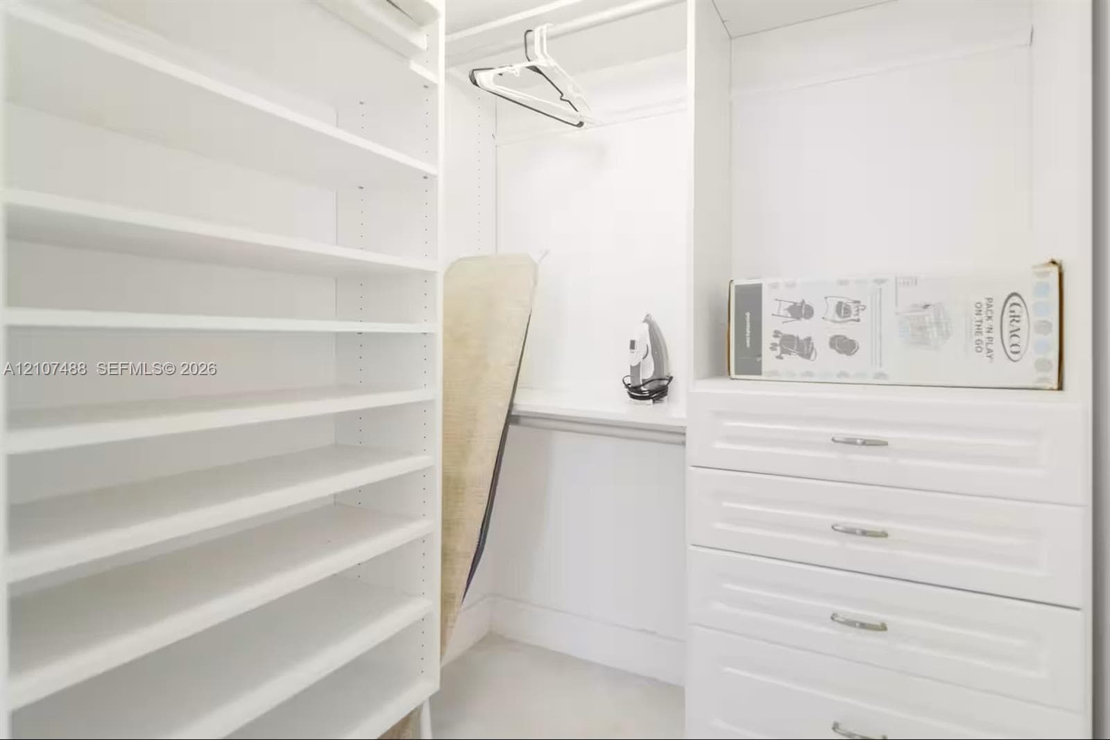 Custom built-in closet featuring white cabinetry, floor-to-ceiling adjustable shelving, integrated storage drawers with metal hardware, and overhead hanging rods