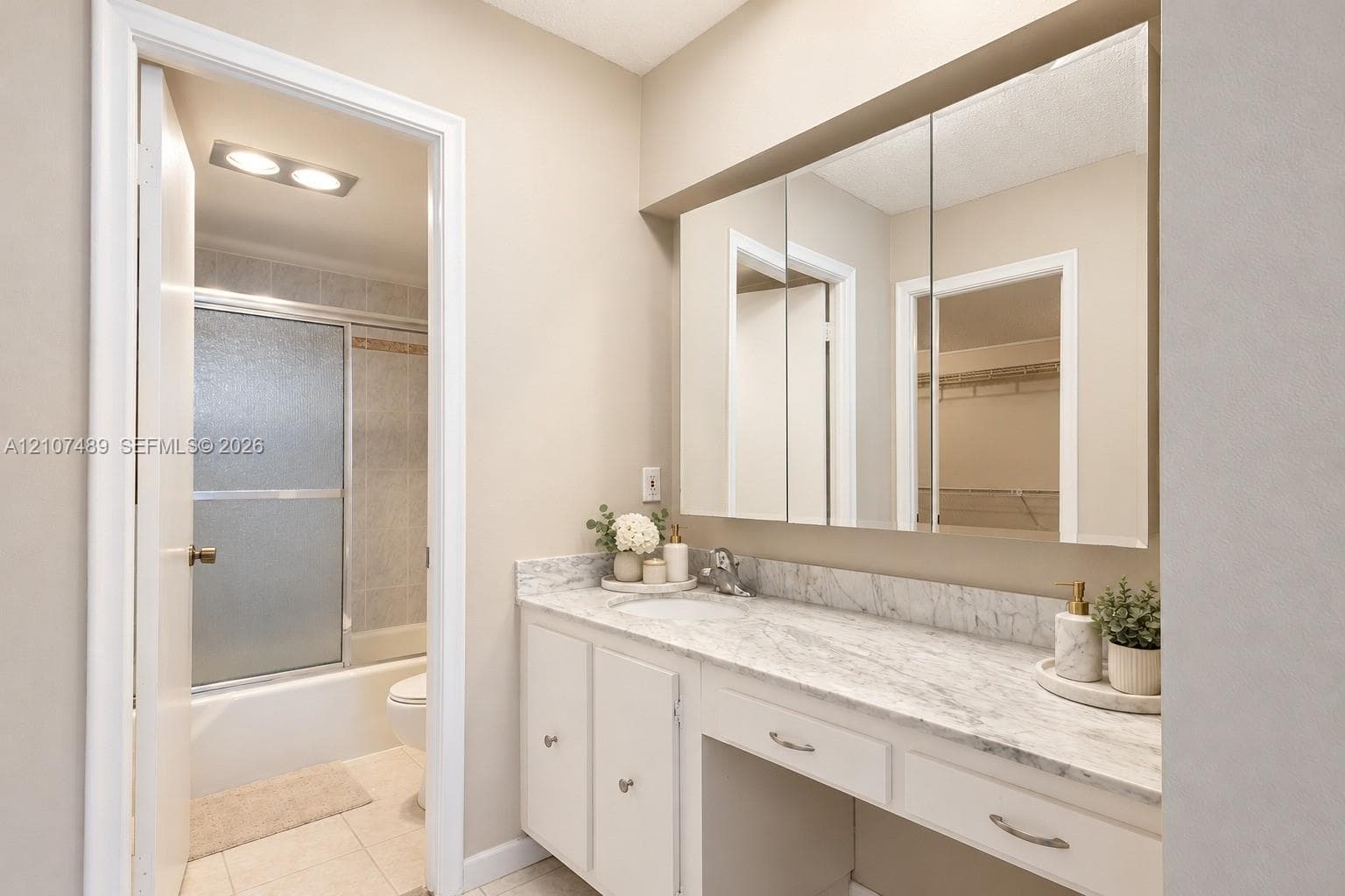 Vanity featuring a stone-look countertop, integrated sink, built-in medicine cabinet, and a dedicated seated vanity space, complete with a separate area containing a tub-shower combination with sliding glass doors
