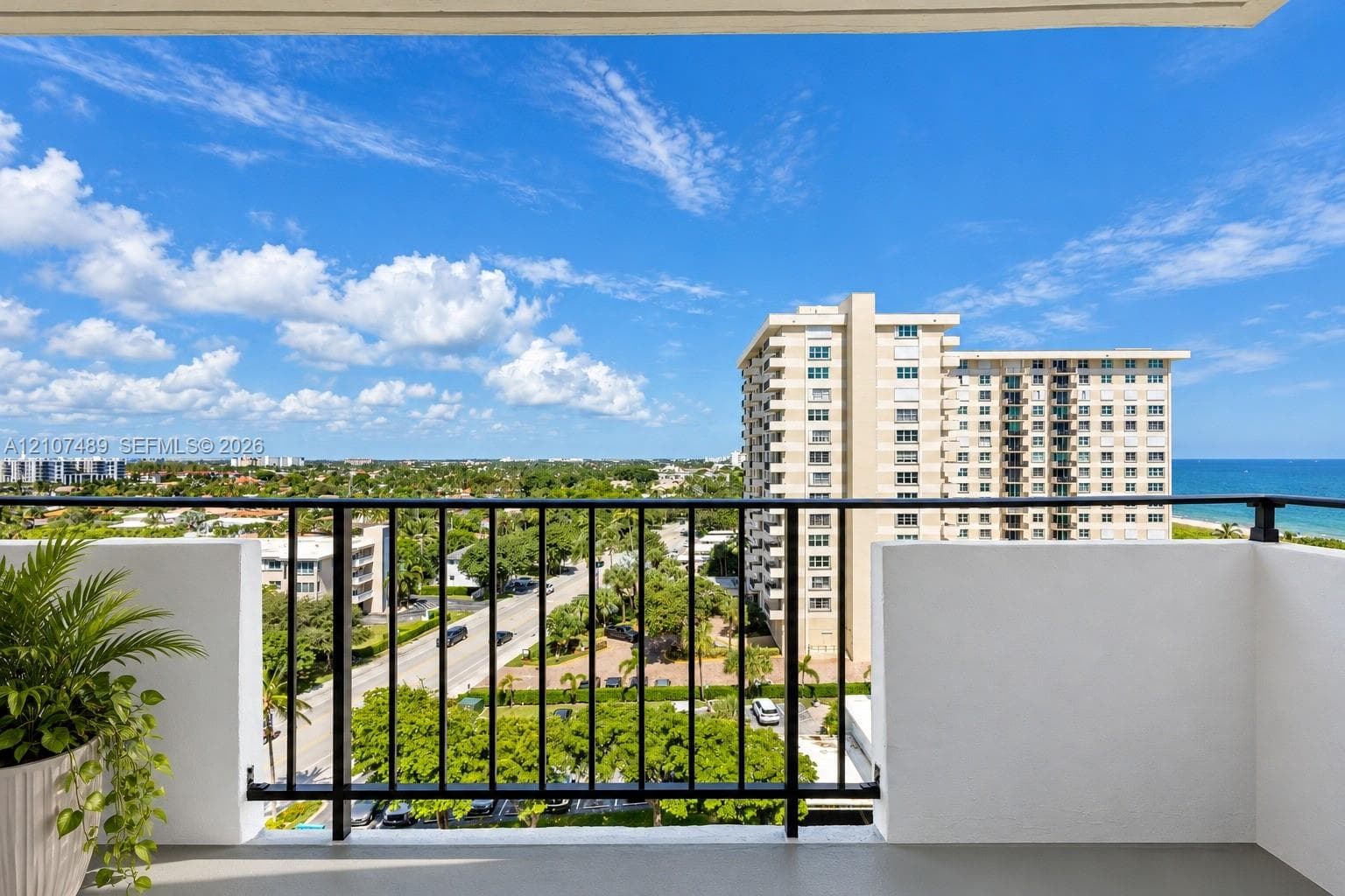 Private balcony featuring a black metal railing and concrete flooring, overlooking the coastline and urban landscape