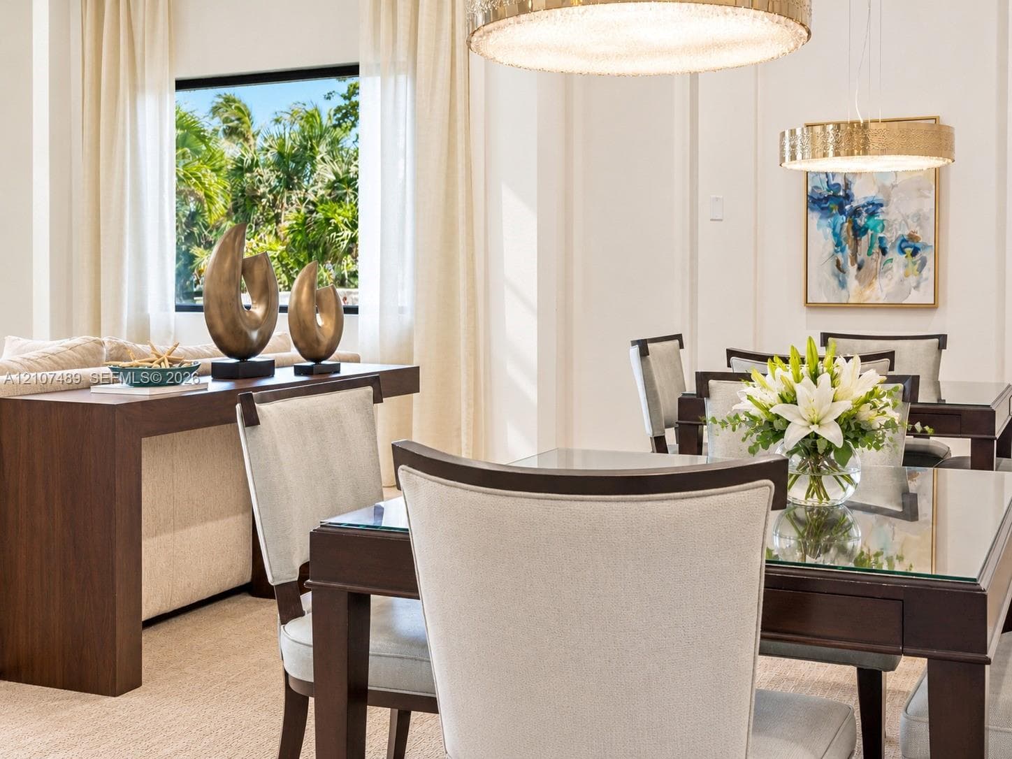 High ceilings with crown molding, dual gold-tone circular pendant lights, and large windows with greenery
