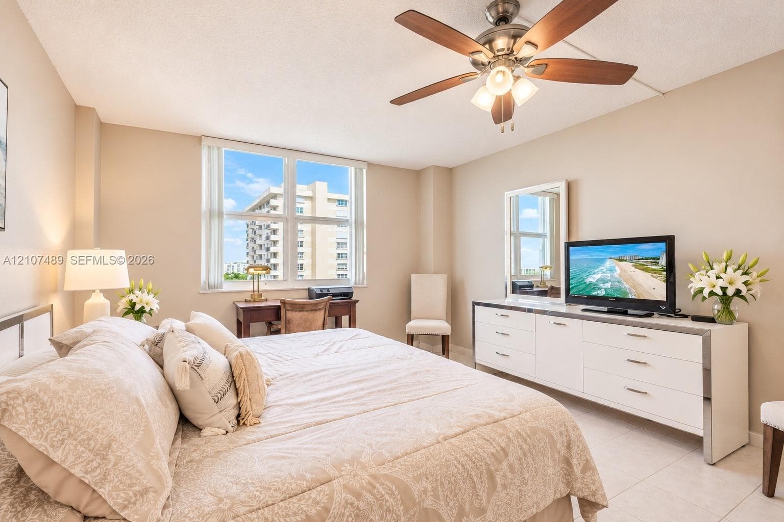 Neutral-toned room featuring large windows, light-colored tile flooring, and a ceiling-mounted fan with integrated lighting