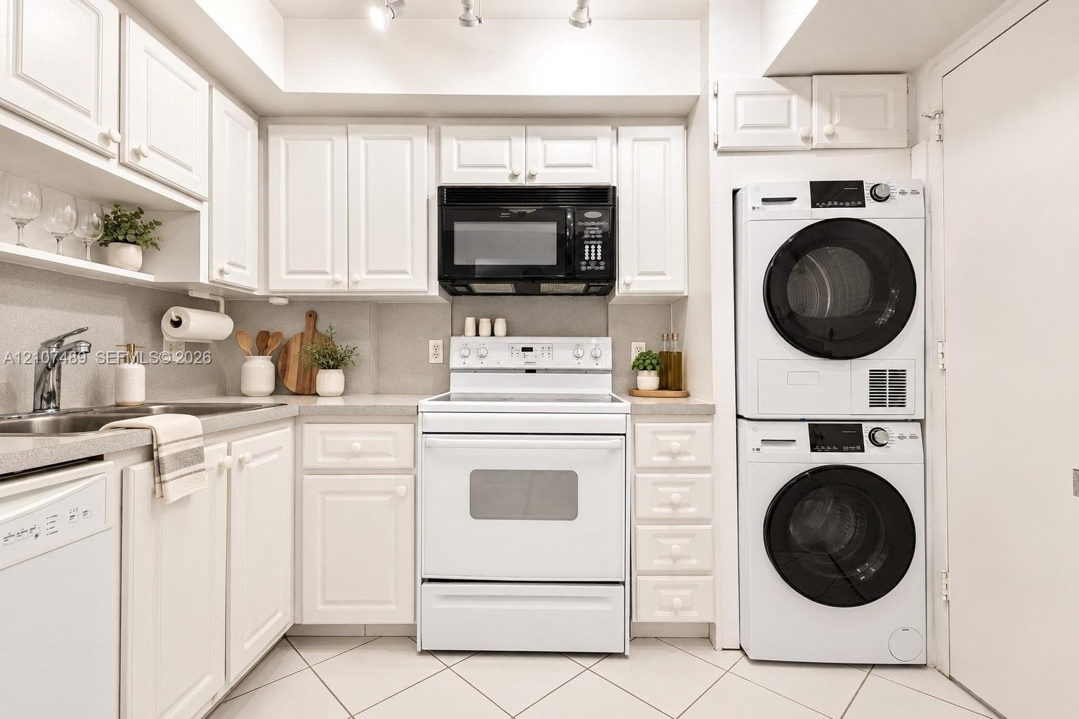 Kitchen featuring shaker-style cabinetry, solid-surface countertops, stainless steel sink with high-arc faucet, integrated laundry center, and tile flooring