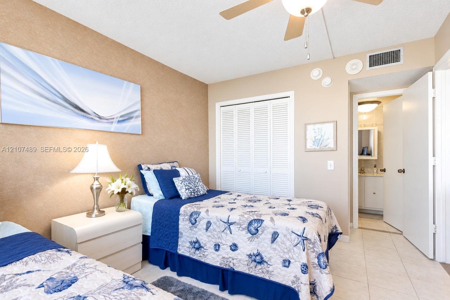 Bedroom featuring textured accent wall, louvered-door closet, ceiling fan with integrated lighting, and tile flooring